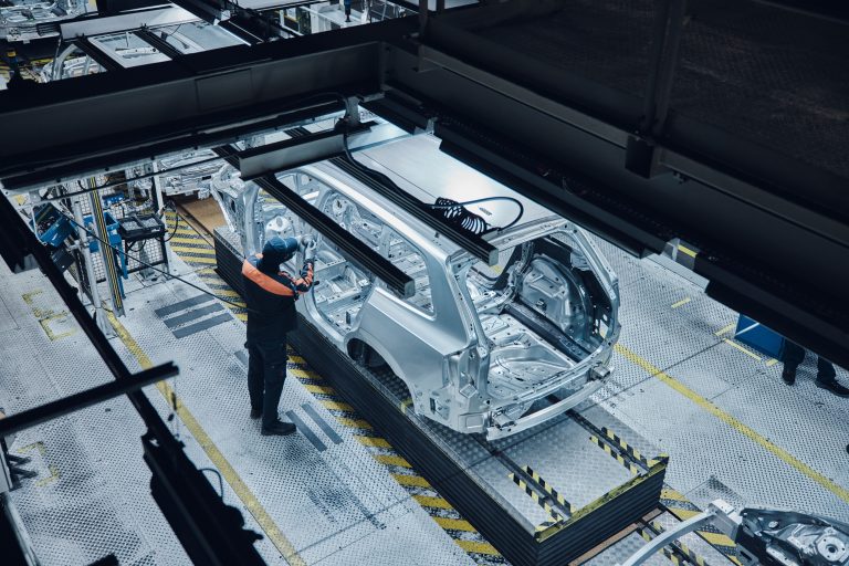 A factory worker inspects a partially assembled car frame on an automotive production line. Credit: Volvo Cars
