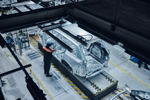 A factory worker inspects a partially assembled car frame on an automotive production line. Credit: Volvo Cars